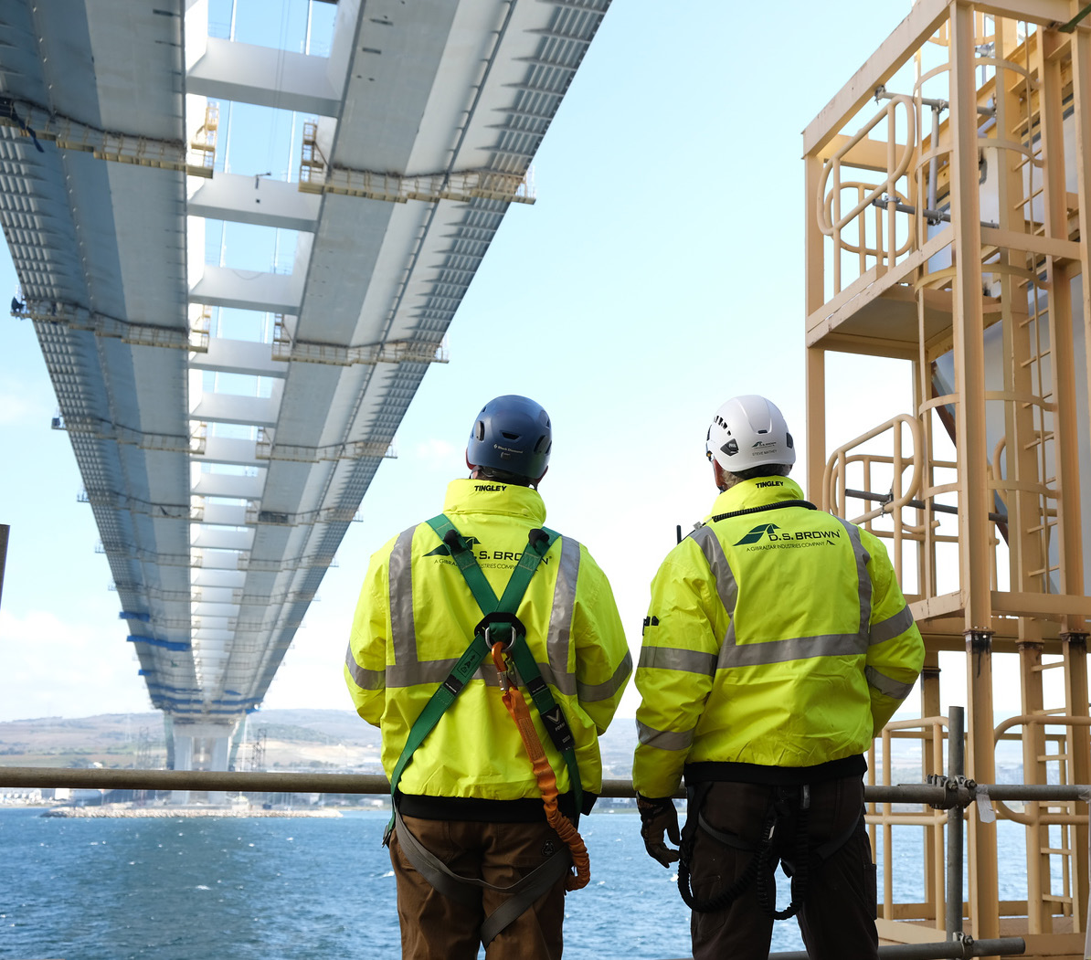 Two D.S. Brown crew members beneath a suspension bridge span